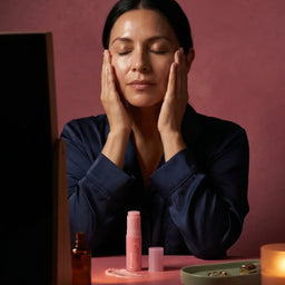 Young woman in purple sweatshirt rubbing Yubiskin product between her palms, seated on a pink stool